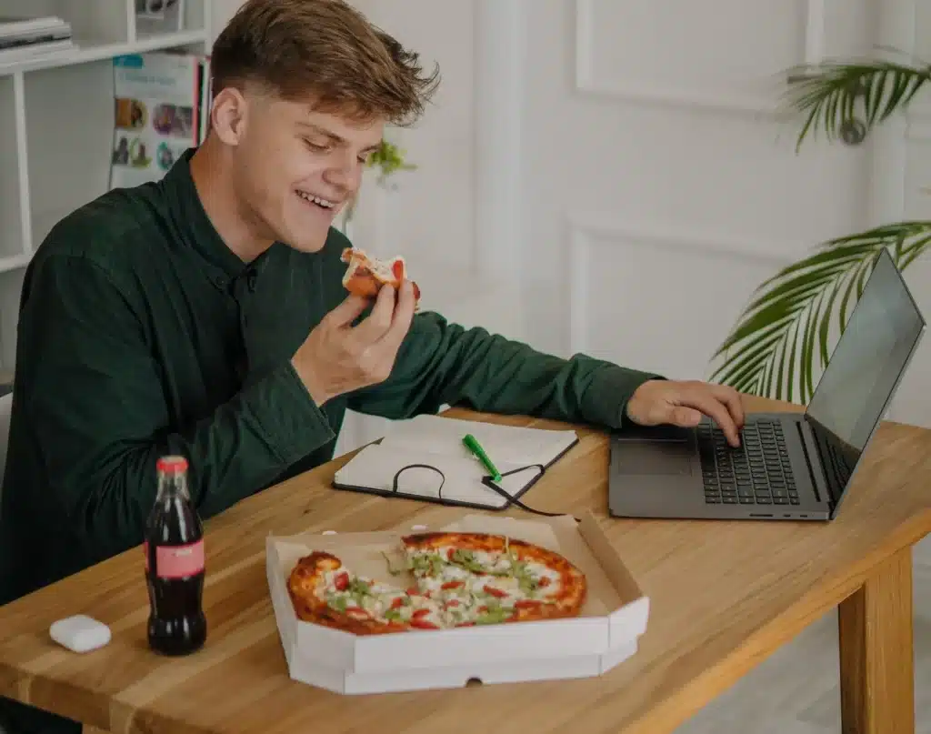 Mann arbeitet von zu Hause und isst dabei Pizza